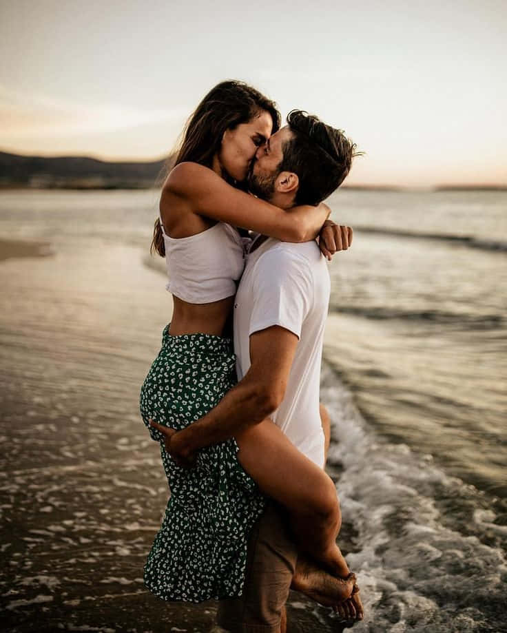 ビーチで波の中を抱き上げられキスするカップルの写真 壁紙
