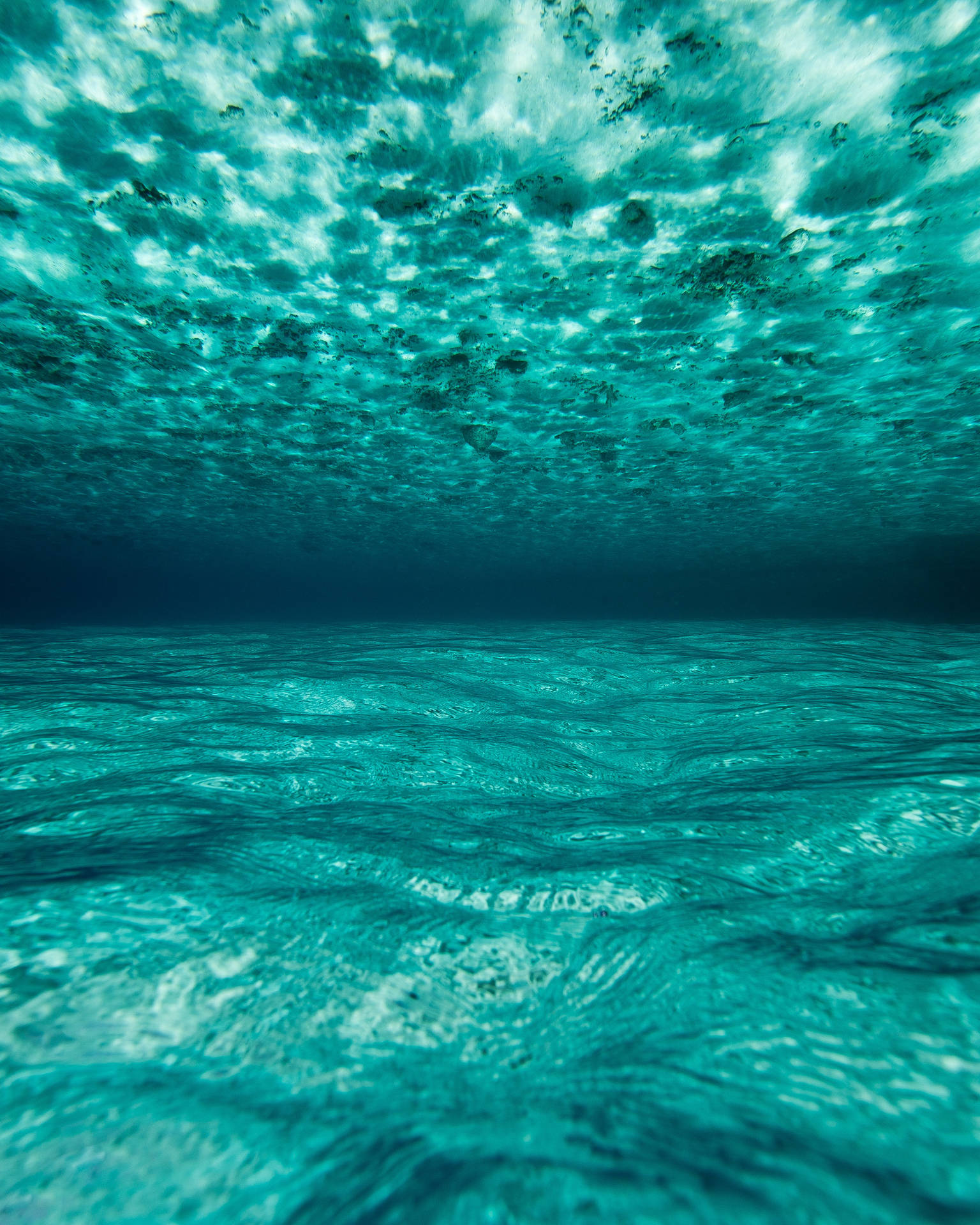 モルディブの透き通った青い海、水中からのショットで水面に太陽の光が反射している様子。