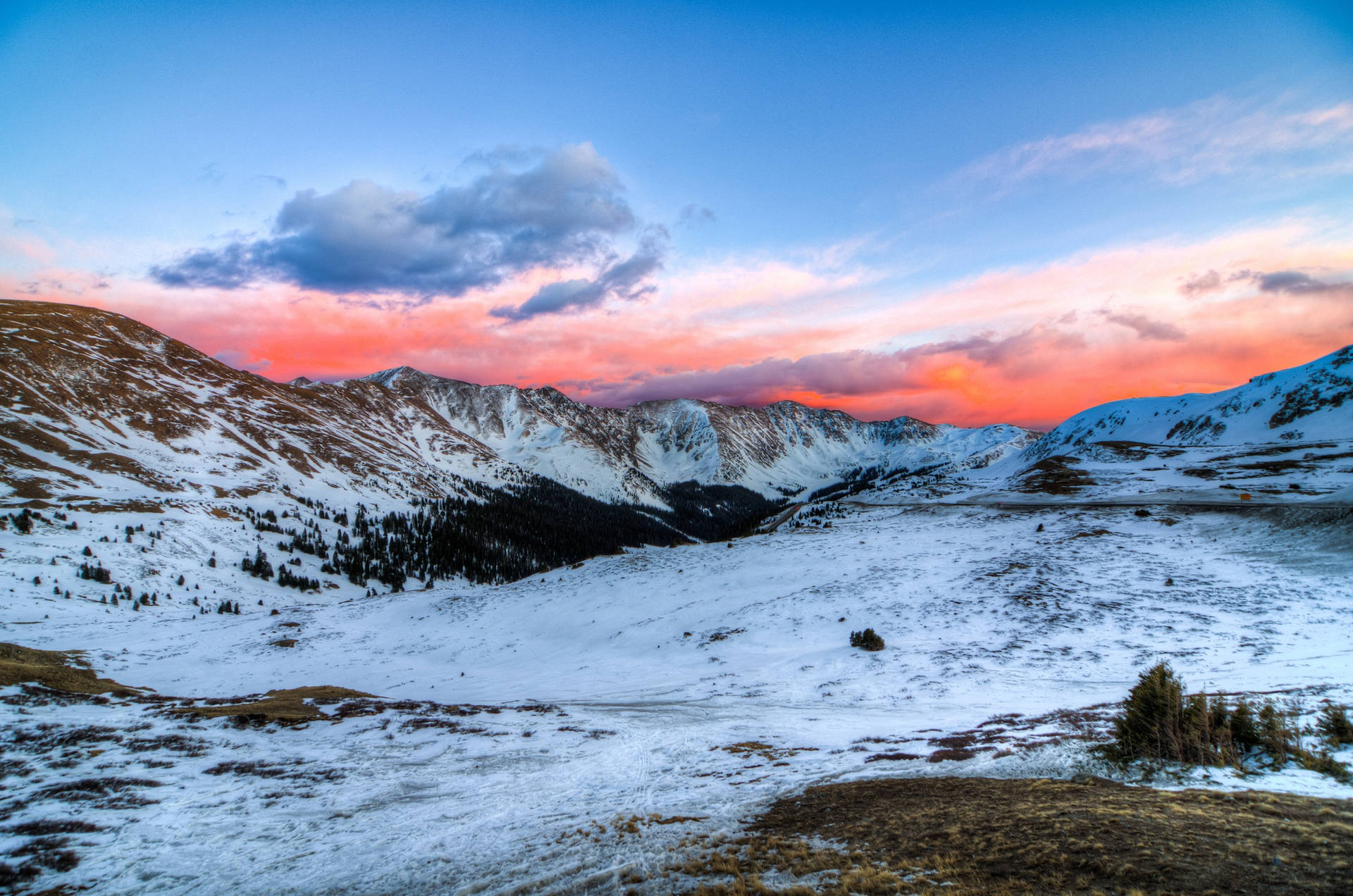 雪に覆われた大地とオレンジ色の空が広がる山の夕焼け。