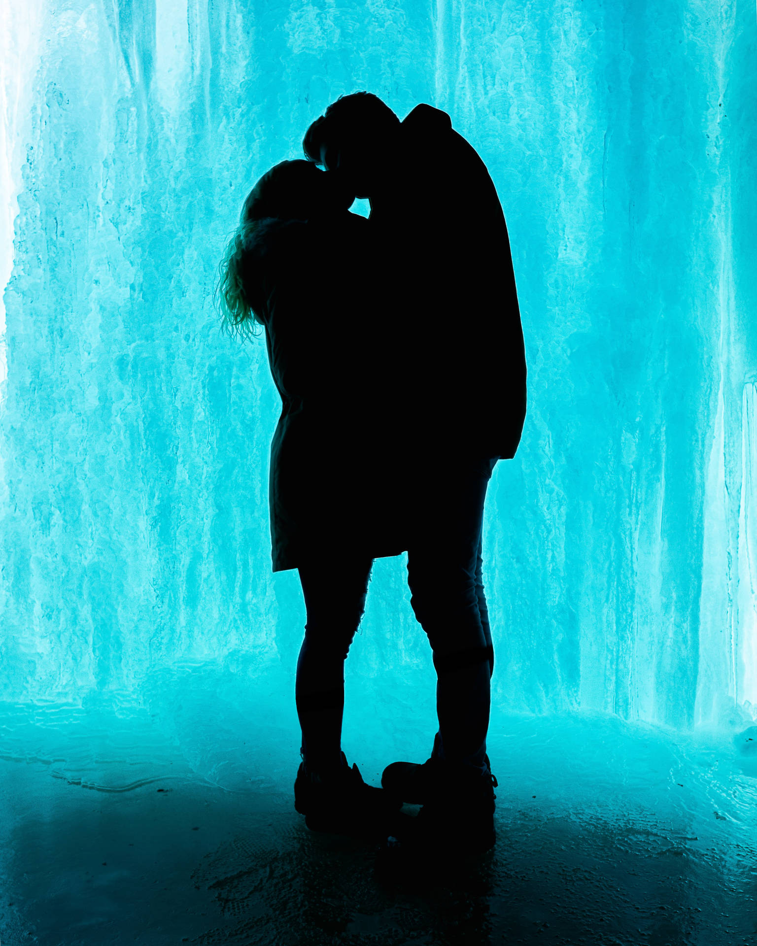 青い氷の背景にキスするカップルのシルエット。バレンタインデーのキスする恋人たち。