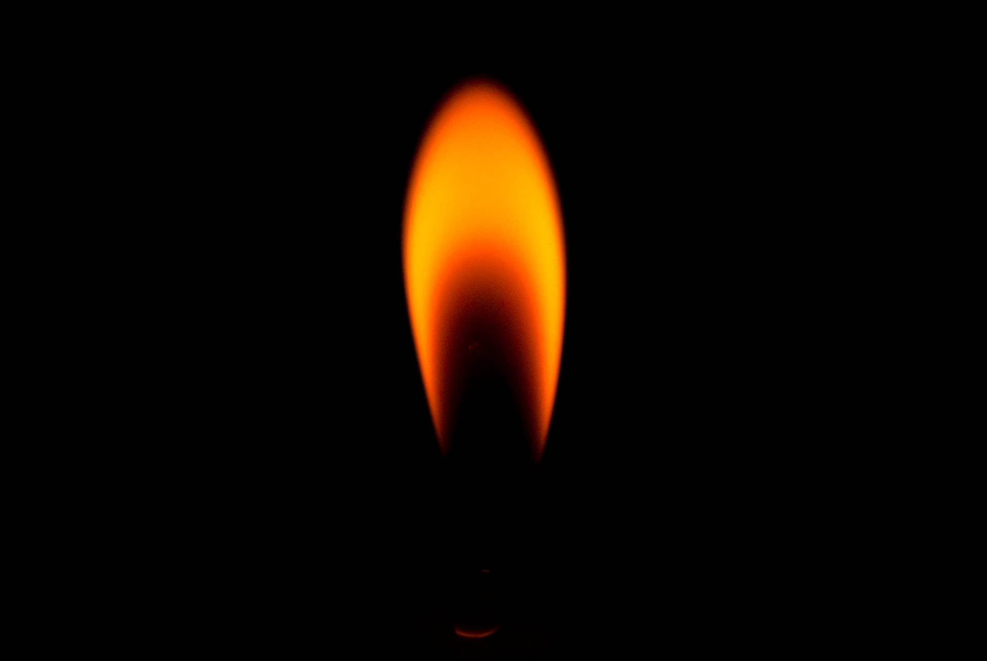 暗い背景に、明るい赤とオレンジ色の炎を上げる小さな芯の火