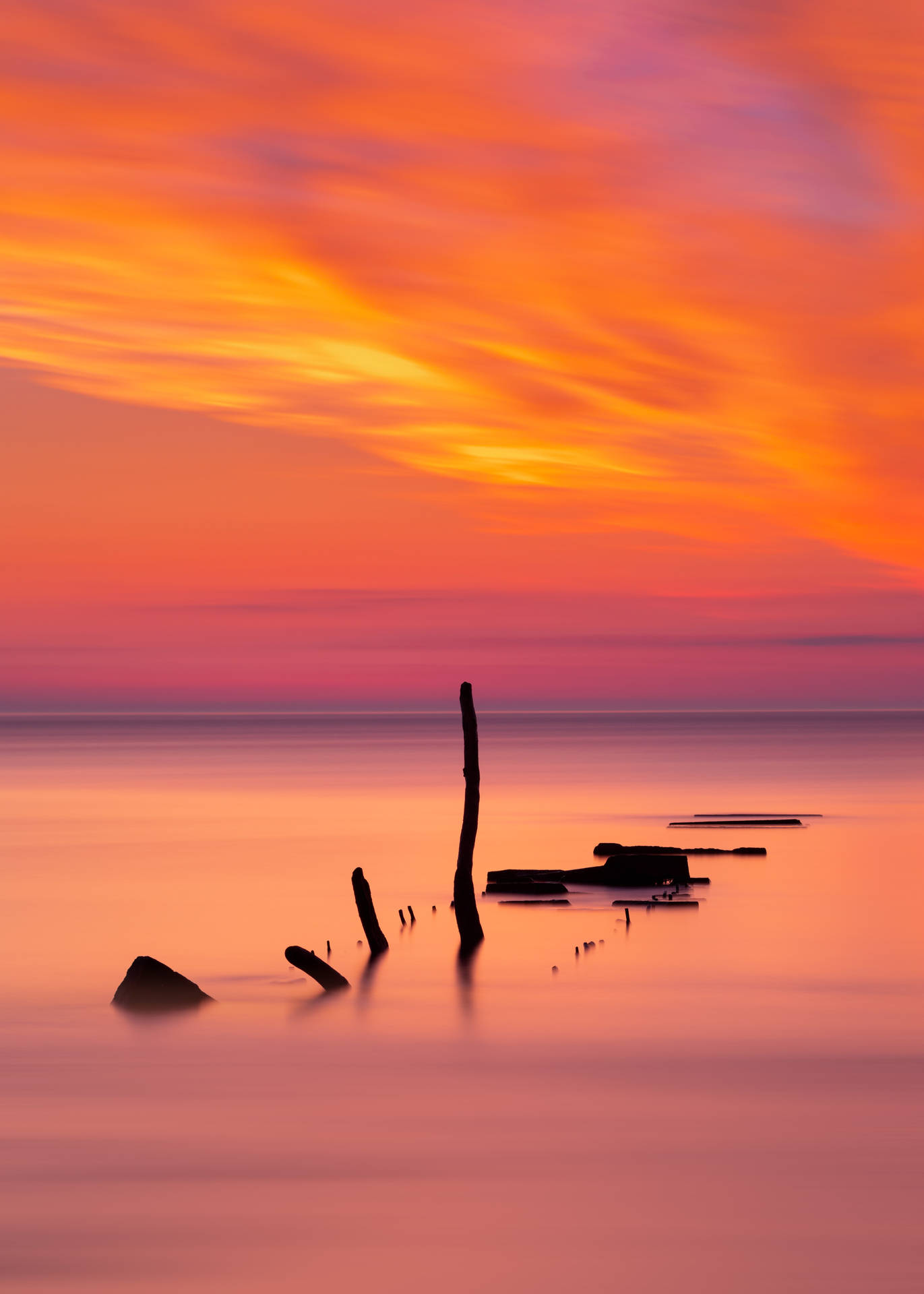オレンジとピンクの水平線の夕日と、浮かぶ棒のある海。