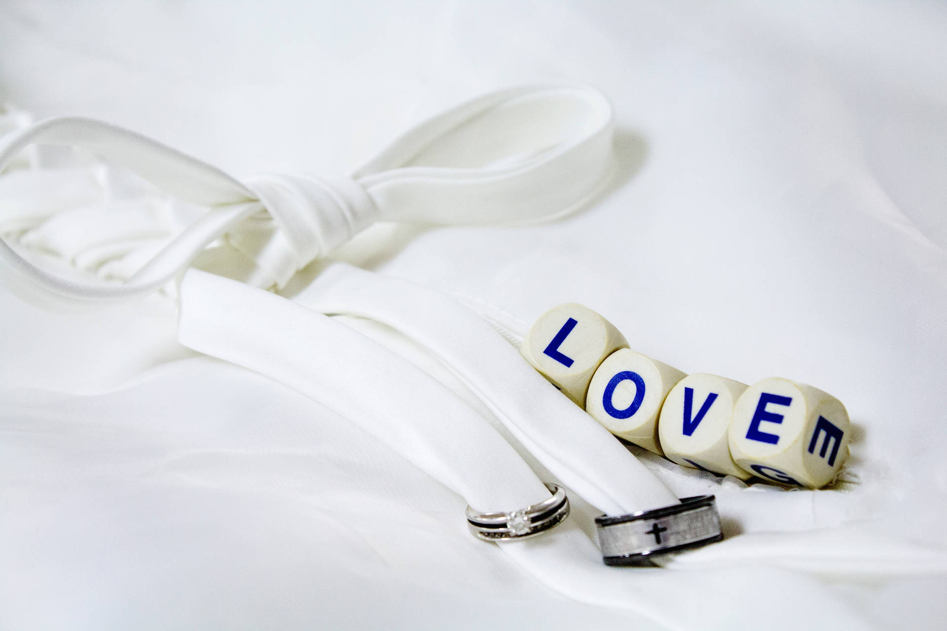 白いシートの上に白いリボンで結ばれた銀と黒の結婚指輪のそばに、「Love」と書かれた4つの白いサイコロ。