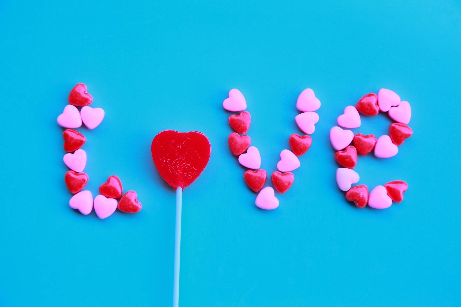 バレンタインデーのために、鮮やかな青い壁に「love」という言葉を作るピンクと赤のキャンディハートの石。