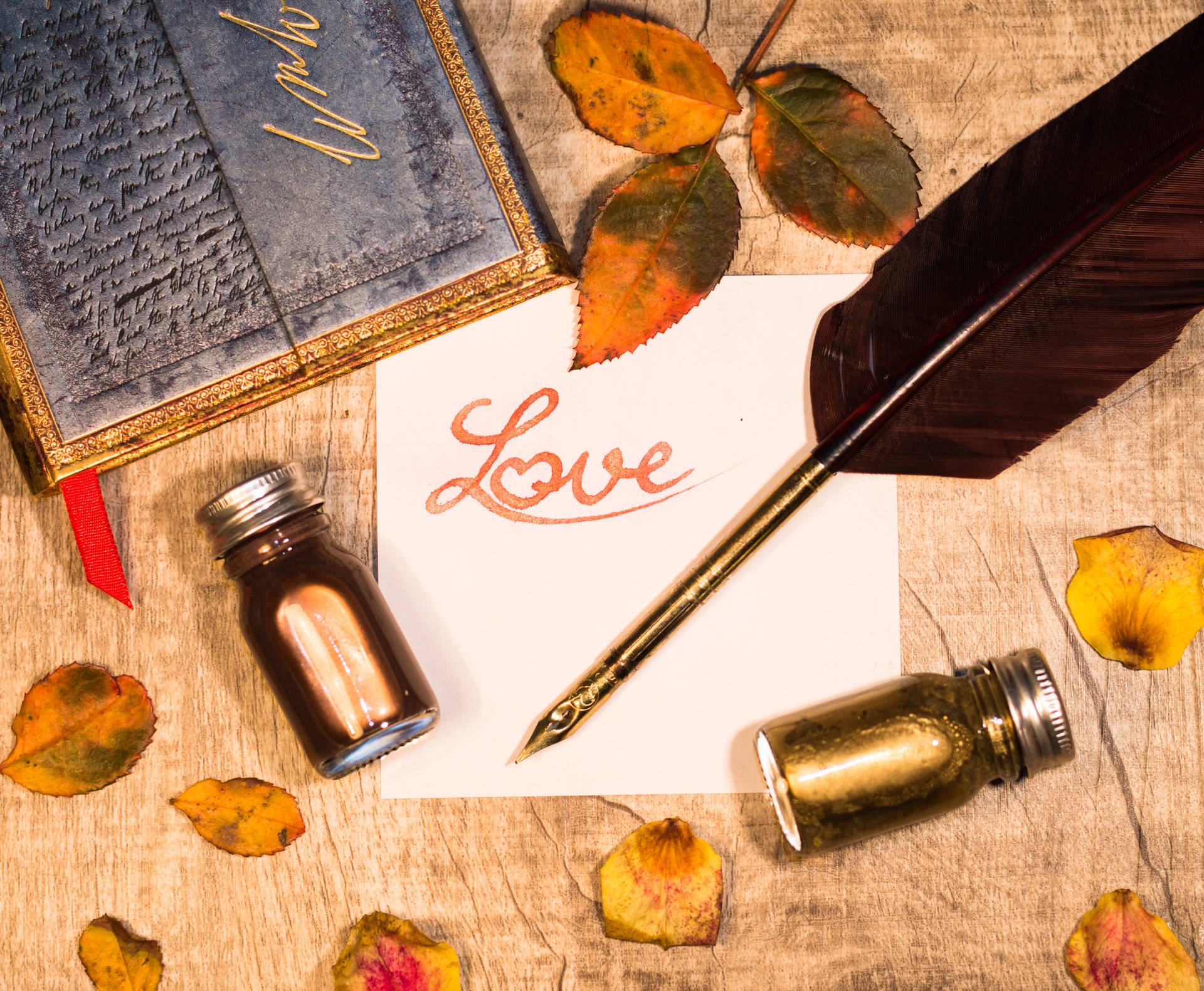 木製のテーブルの上に、羽根ペンとインク瓶とともに白い紙に書かれたオレンジ色の「Love」の文字。バレンタインデーのラブレター。