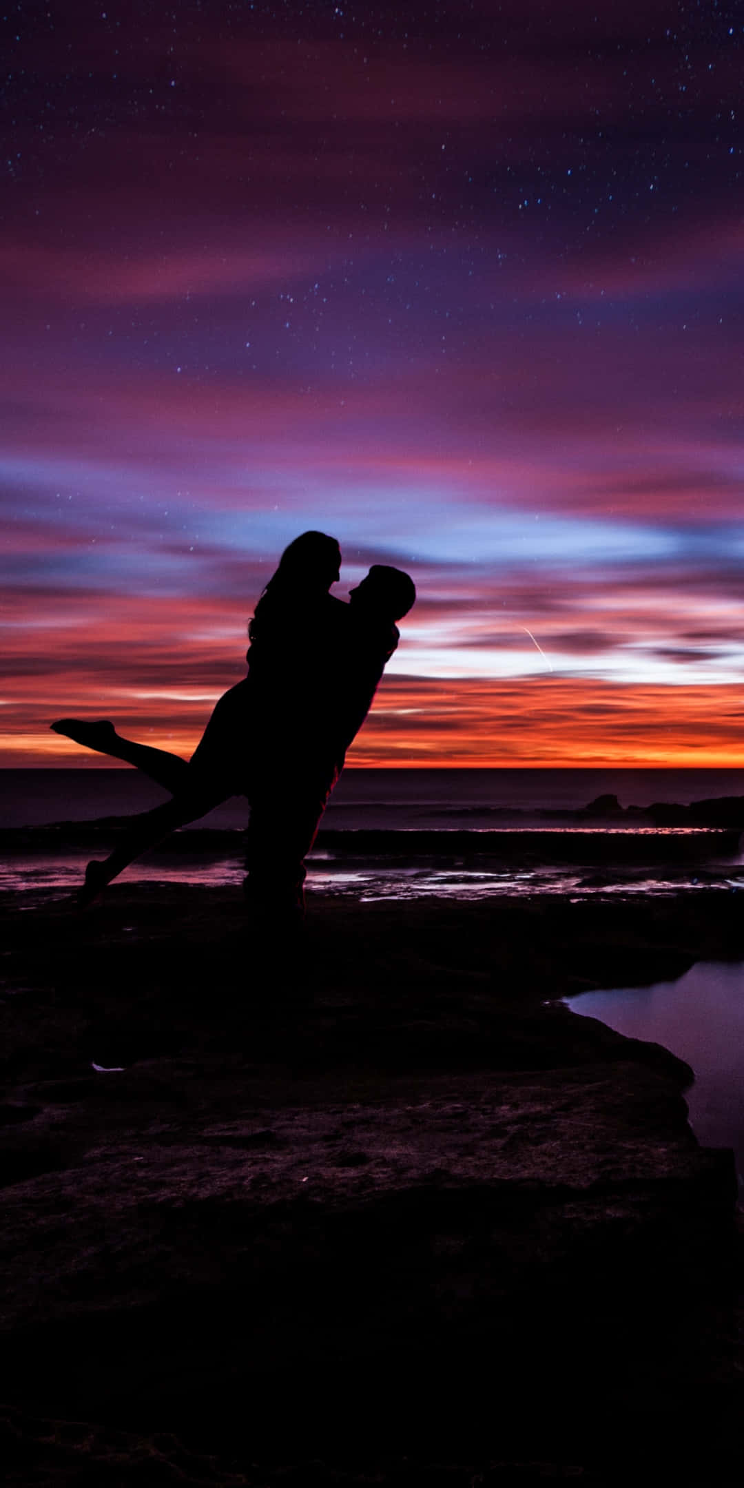 紫色の夕焼け空の下で女性を抱えるカップルの写真 壁紙