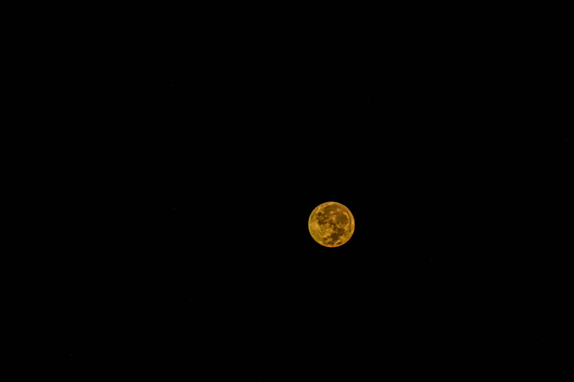 真夜中の暗い空に浮かぶ黄色い月。暗闇の中で明るく輝く。