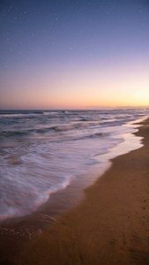 夕暮れ時の穏やかなビーチの風景。パステルカラーの空と優しい波が広がる、落ち着いた壁紙。