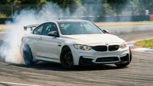 白いBMW M4がサーキットのカーブをドリフトで曲がり、タイヤの煙とモーションブラーが生じている。 — BMW 壁紙