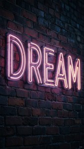 夜のレンガ壁に輝く「DREAM」のネオンサイン、ムーディーでアーティスティックな雰囲気。 — iPad 壁紙