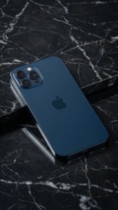 大理石の上に置かれたミッドナイトブルーのiPhone 17、ミニマルなスタジオショット。