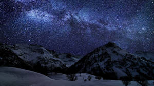 雪をかぶった山並みと星々の壁紙。