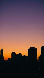 紫色とオレンジ色の空が広がる夕暮れ時の都市景観。都会的な雰囲気のiPhone用壁紙。 — iPhone エステティック 壁紙