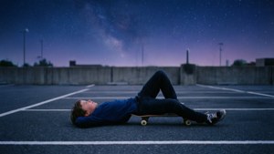 静かな空き地で星空の下でくつろぐスケートボーイ。