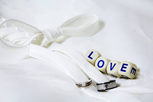 白いシートの上に白いリボンで結ばれた銀と黒の結婚指輪のそばに、「Love」と書かれた4つの白いサイコロ。