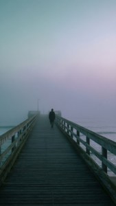 夜明けの霧に包まれた桟橋に立つ一人の人影。落ち着いたティールとラベンダーの色調。 — 美的なアートGIF 壁紙